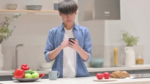 Young Man Using Smartphone in Modern Kitchen