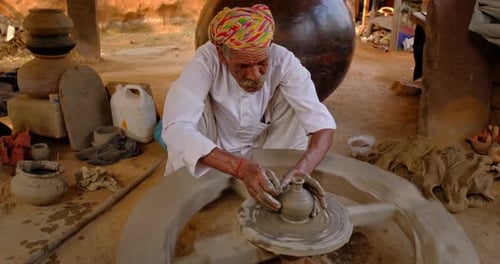 Potier indien au travail : lancer le volant du potier et façonner un récipient en céramique et des articles en argile : pot