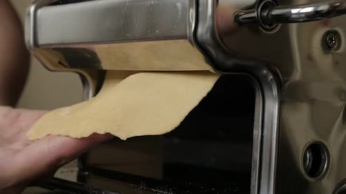 Hands feeding dough through a pasta machine