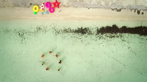 Aerial view of friends playing with ball in transparent sea by sandy beach.