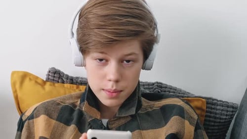 Teenager Wearing Headphones Using Mobile Phone at Home
