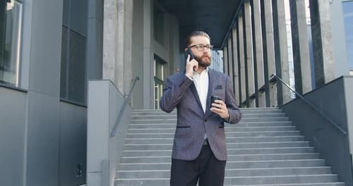 Office Manager with Glasses in Business Clothes which Drinking Coffee and Talking on Smartphone
