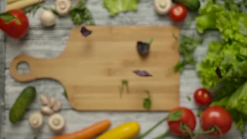 Parsley and Basil Leaves Falling on Wooden Cutting Board