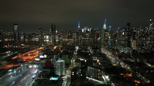 An aerial view from high over Long Island City, New York at night. The drone camera slowly dolly out