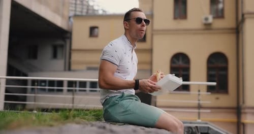 Man Eating Food Sitting in a City