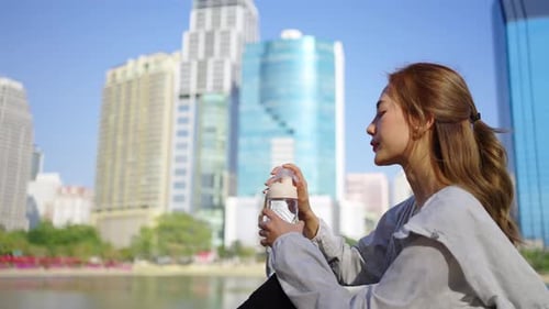 4K Asian woman drinking water from a bottle while jogging at public park in the morning.