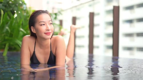 Nahaufnahme einer jungen Frau, die im seichten Wasser in einem Pool auf dem Dach eines Resorts liegt. Space im Titel