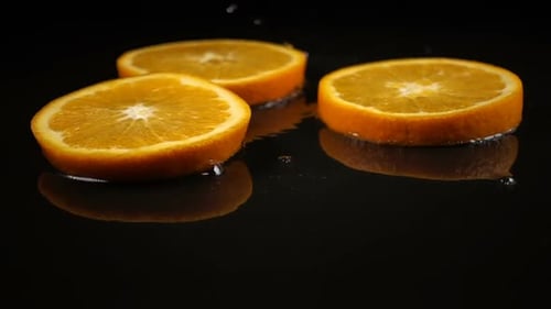 Orange Slices Fall on the Black Surface Covered with Water