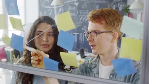 Young Colleagues Drawing Diagram on Glass Wall in Creative Agency