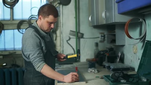 Man Hammering Punch in Workshop
