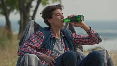 Young Man Relaxes Outdoors and Drinks Refreshment