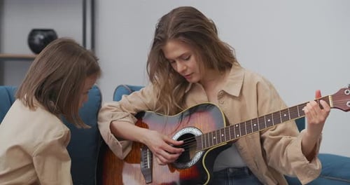 Woman Plays Guitar for Child on Couch