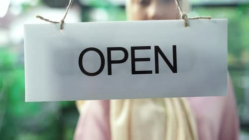 young cafe owner turning storefront sign from close to open and welcoming customers at cafe.