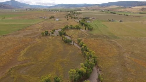 Aerial view flying over winding dry riverbed with trees