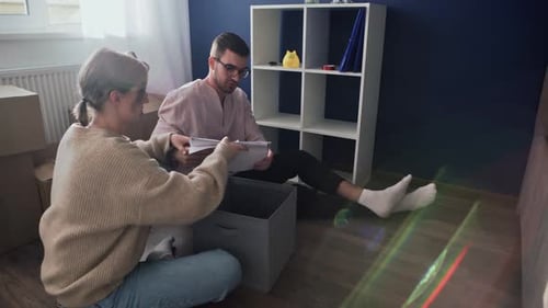 Happy Couple Open Packing Cardboard Boxes After Relocation Family Sitting on Floor in Living Room