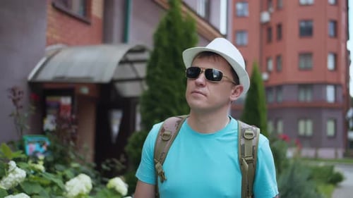 Young male tourist walks around the city wearing hat and sunglasses, camera tracking