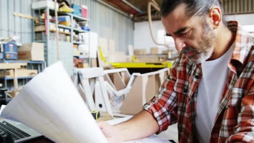 Man Examines Blueprint at Workshop with Technology
