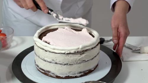 Baker Applying Pink Frosting to Chocolate Cake