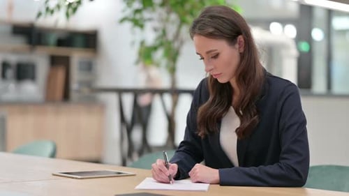 Woman Writing at Desk in Modern Office Setting