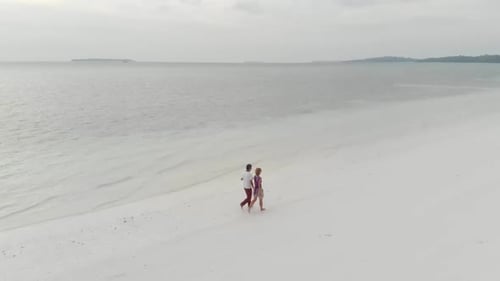 Aerial slow motion: couple on vacation walking on exotic beach romantic sky