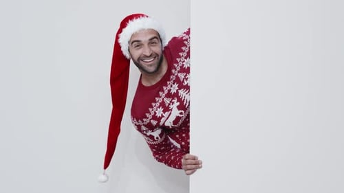 Cheerful Man in Santa Hat Peeking From Behind Wall