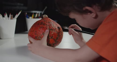 Child Paints Cheerful Face on an Orange Pumpkin