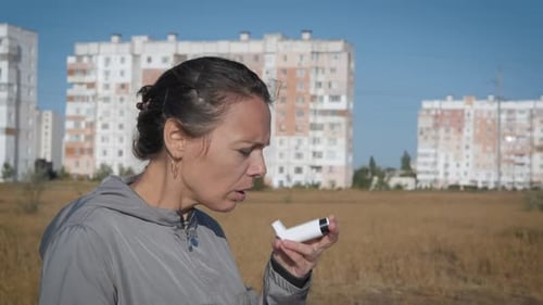 Woman Uses Inhaler Outdoors in Urban Setting