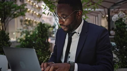 Man with Beard Types on Laptop at Outdoor Cafe