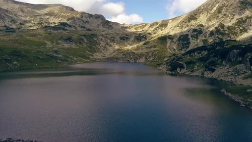 Wide aerial drone slowly flying over a lake towards a mountain range.