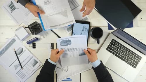 Top View Male Hands of Two Young Businessmen Checking Graphs and Discussing Financial Reports in