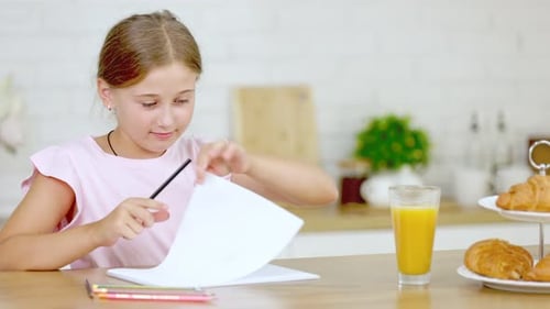 Niña dibuja mientras está sentada en la cocina