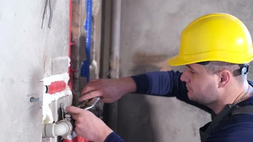 Construction Worker Tightens Fixture on Exposed Pipes