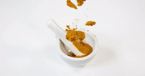 Currypulver fällt in einen Mörser und Stößel vor weißem Hintergrund, Zeitlupe 4K