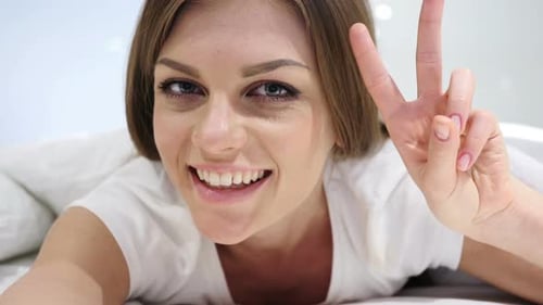 Woman Smiling and Giving Peace Sign in Bed