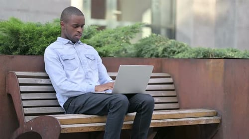 Man Using Laptop on Bench Coughs, Feels Ill