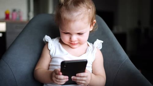 Adorable Child Using Mobile Phone in Chair