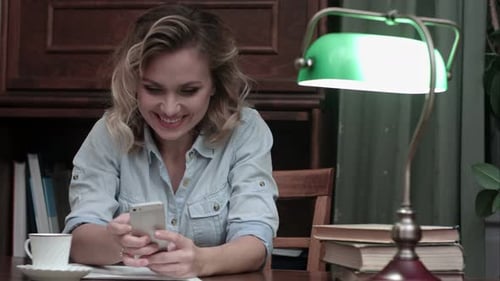 Smiling Woman Uses Smartphone at Desk Indoors