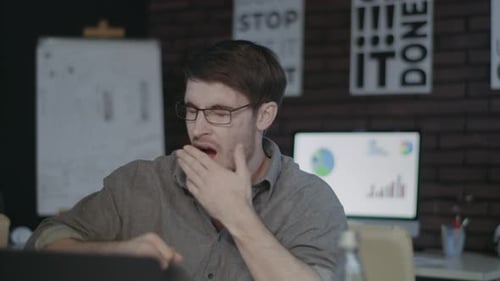 Tired Business Man Stretching Hands and Yawning in Front Laptop in Night Office