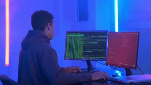 Young Adult Coding on Computer in Neon Lit Room
