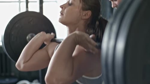 Woman Lifting Weights with Trainer Assistance in Gym