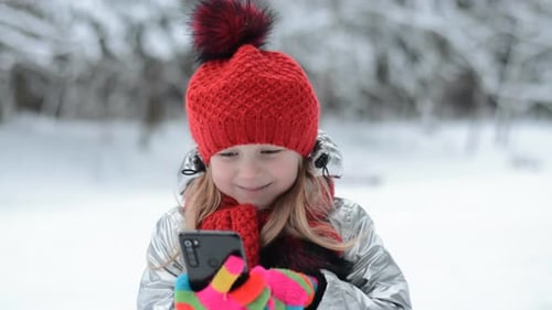Little Caucasian Girl Portrait in Winter Park Writes a Message on a Smartphone
