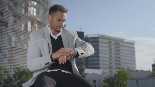 Man Sitting Outside, Checking Watch in Urban Setting