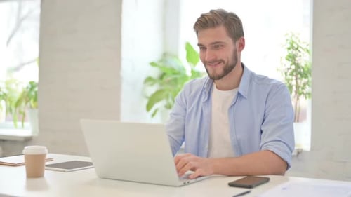 Successful Young Creative Man Celebrating on Laptop in Modern Office