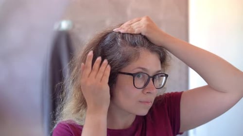 Woman Examines Gray Hair in Mirror Close Up