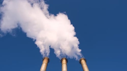 Factory Smokestacks Emitting Billowing Smoke Against Blue Sky