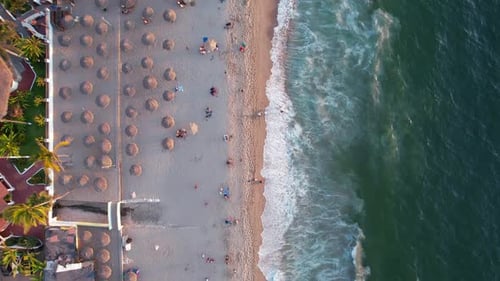 tourists at Los Muertos Beach with straw umbrellas at sunset in Puerto Vallarta Mexico, aerial top d