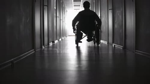 Silhouette of Man Riding on Wheelchair along Corridor