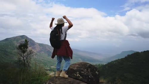 Backpacking female hiker stands on top of the mountain and enjoying the view.