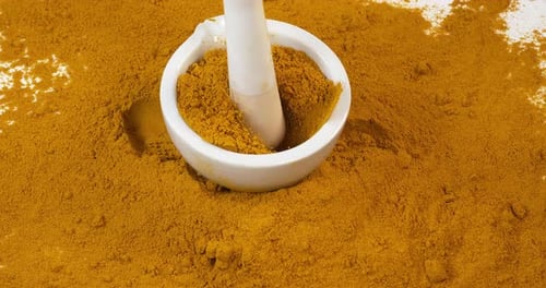Currypulver fällt in einen Mörser und Stößel vor weißem Hintergrund, Zeitlupe 4K