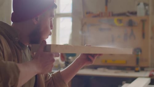 Man Inspecting Wood Plank in Sunny Workshop